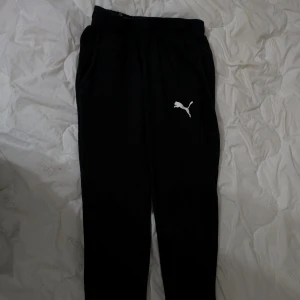 Svarta mjukisbyxor från Puma - Säljer ett par svarta mjukisbyxor från Puma med elastisk midja och det klassiska Puma-logotypen på benet. Perfekta för en avslappnad stil eller träning.