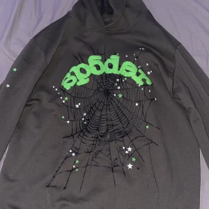  Hoodie spider Hoodie 555 - Cool svart hoodie med ett stort grönt 'sp5der' tryck och spindelnätsdesign. Hoodien har långa ärmar och små stjärnor i grönt och vitt som detaljer. Perfekt för en unik och avslappnad stil.
