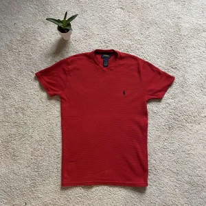 Röd t-shirt från Polo Ralph Lauren - Snygg röd t-shirt från Polo Ralph Lauren med klassisk passform. Den har en liten broderad logga på bröstet och är tillverkad i ett bekvämt material. Perfekt för en stilren look med en strä bomulls material.