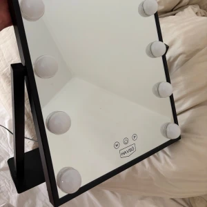 Sminkspegel med belysning  - Snygg sminkspegel med inbyggd belysning. Spegeln har en svart ram och 12 runda lampor som ger bra ljus för sminkning. Spegeln är justerbar och kommer med en strömadapter. Den har tre olika ljus inställningar, varma och kalla och även dimbara.  Det är två pluppar som ramlat av lampan men de lamporna fungerar som vanligt ändå, jag har plastbitarna till vet bara inte hur man sätter på de igen.