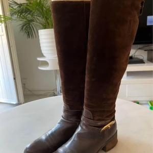 Bruna ridstövlar med dragkedja - Snygga bruna ridstövlar i mocka och skinn med dragkedja baktill. Perfekta för ridning och höstväder. De har en låg klack och en stilren design.                            