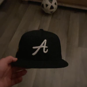 Svart keps med broderad bokstav - Snygg svart keps med en vit broderad bokstav 'A' på framsidan. Perfekt för en casual look. Justerbar passform baktill.