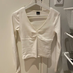 Vit långärmad topp från Gina Tricot - Snygg vit långärmad topp från Gina Tricot med v-ringning och rynkdetalj framtill. Perfekt för en stilren look. I storlek s. Har Max använt den 3 gånger, skicka dm för mer bilder😊