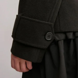 Svart kappa med knappar - Snygg svart kappa med dubbelknäppning och breda slag. Jackan har långa ärmar med dekorativa knappar vid ärmsluten. Perfekt för en stilren look. Helt ny me lapp kvar 