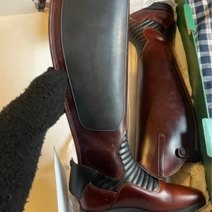 Bruna ridstövlar i skinn - Eleganta bruna ridstövlar i skinn med svarta detaljer. Stövlarna har en stilren design med elastiska partier för bättre passform och komfort. Perfekta för ridning och ger ett klassiskt intryck.Helt nya globus stövlar storlek 39, dock behöver dragkedjan bytas på ena :) 