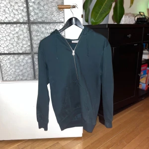 Weekday Zip up - Säljer en stilren mörkgrön hoodie från Weekday i storlek XS. Den har en dragkedja framtill och en klassisk huva. Perfekt för en avslappnad look. Sitter ej som XS, mera som S-M