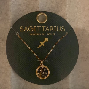 Guldhalsband med Skyttens stjärntecken - Elegant guldhalsband med ett hänge som visar Skyttens stjärntecken. Perfekt för den som är född mellan 22 november och 21 december. Hänget har en fin detalj med stjärnor och en pil, vilket ger en personlig touch.