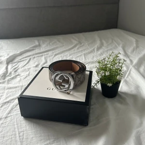 Mönstrat bälte med silverdetaljer från Gucci - Snyggt bälte från Gucci med ett klassiskt mönster och en stor, rund spänne i silver. Bältet har en stilren design med en brun insida och mönstrad utsida. Perfekt för att ge en lyxig touch till din outfit. Den är sönder lite men funkar jätte bra ändå. Man behöver inte ta bältet igenom första flärpen där den är sönder!
