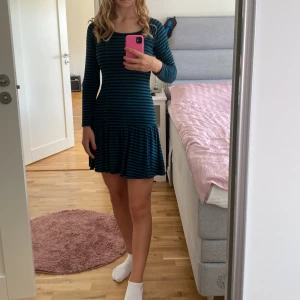 Randig klänning från ZARA - Säljer en superfin randig klänning från ZARA. Den är svart och blå med knappar framtill och har en volangdetalj längst ner. Klänningen har trekvartsärmar och är perfekt för både vardag och fest!