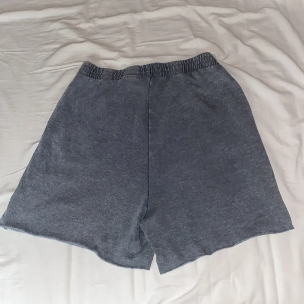 Säljer ett par grå shorts med elastisk midja och coolt tryck på ena benet. Perfekta för en avslappnad dag eller en tur till stranden. De är i bra skick och superbekväma!. Shorts.