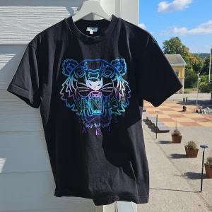 Svart t-shirt med tigertryck från Kenzo - Säljer en svart t-shirt från Kenzo i storlek XS men skulle säga att den är åt det större hållet för att vara XS. Broderad logga på framsidan. Tröjan är i fint skick och bara använd några gånger 