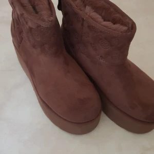 Bruna mocka boots från Guess - Säljer ett par snygga bruna boots från Guess i mocka. Stolek 35. De har en bekväm platåsula och ett diskret mönster på skaftet. Perfekta för höst och vinter med sin varma mjuka insida.Använda 2 gånger är för stora för mig.