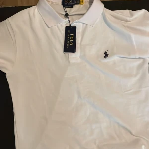 Vit pikétröja från Polo Ralph Lauren - Säljer en klassisk vit pikétröja från Polo Ralph Lauren. Den har en broderad logga på bröstet och en stilren krage. Perfekt för både vardag och lite finare tillfällen. Tröjan är i nyskick och redo för en ny ägare!