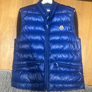 Moncler väst - Tjena säljer min Moncler Gui. I denna sällsynta färgen. 2 mindre hål vid halseninget som släpper ut något ludd. Skick 8/10 utan hålen Size 5 M/L Blå Skick