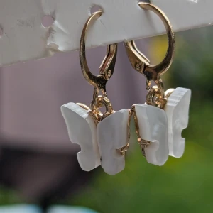 Vita fjärilsörhängen med gulddetaljer - Superfina örhängen med vita fjärilar och guldfärgade detaljer. De är formade som små fjärilar och hänger på en guldfärgad ring. Perfekta för att ge en söt och elegant touch till vilken outfit som helst!
