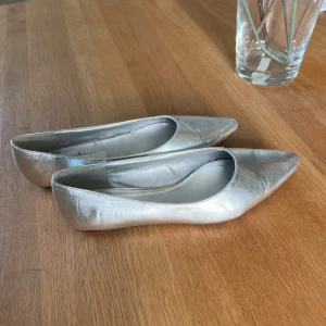 Skor - Super fina silvriga ballerinaskor. Prislapp kvar, endast provade så i nyskick. Dem har dock stått väldigt länge vilket kan göra att dem ser något slitna ut, därav priset. Storlek 39.