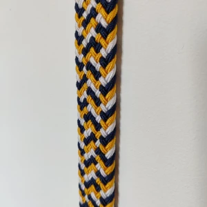 Flerfärgat flätat bälte - Säljer ett snyggt flätat bälte med ett coolt mönster i blått, vitt och gult. Bältet har en brun skinnliknande detalj vid spännet som ger en stilren touch. Perfekt för att liva upp vilken outfit som helst!