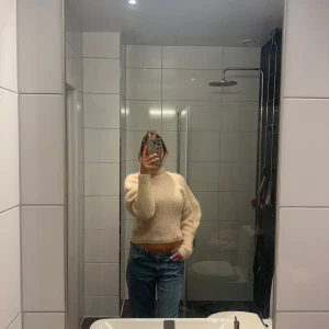 Beige stickad tröja - Säljer en supermysig beige stickad tröja som är perfekt för kyliga dagar. Den har en hög krage och långa ärmar, vilket gör den extra varm och skön. Tröjan är lite croppad och är puffig vilket ger en snygg look. Perfekt för både höst och vinter. 