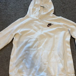 Vit hoodie från Nike - Säljer en vit hoodie från Nike. Den har en klassisk design med en känguruficka och Nike-loggan broderad på bröstet. Perfekt för både vardag och träning! Använd ett fåtal ggr men i bra skick.