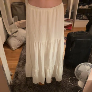 Vit långkjol med slits - Fin vit långkjol med slits på sidan. Underkjol finns alltså inte genomskinlig. Funkar som låg, medel eller högmidjad. 