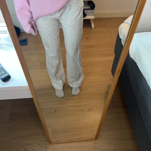 Vita byxor med broderade detaljer - Snygga vita byxor med broderade hålmönster och snörning i midjan. Byxorna har en loose passform och är perfekta för en avslappnad stil. De är högmidjade och tillverkade i ett lätt och bekvämt material.