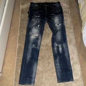Dsquaread 2 jeans  inte äkta - Snygga mörkblå jeans med coola slitningar och färgstänk. De har en straight passform och klassisk femficksdesign. Perfekta för en avslappnad stil med en edgy touch och helt nya 