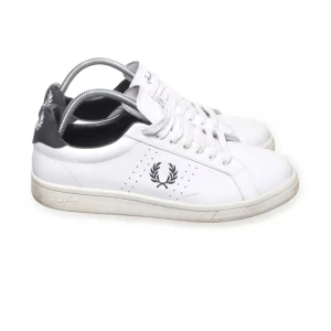 Vita sneakers från Fred Perry - Snygga vita sneakers från Fred Perry med svart häl och klassisk logga på sidan. Skorna har snörning och en stilren design som passar perfekt till vardags. Tillverkade i skinn för en hållbar och bekväm känsla.
