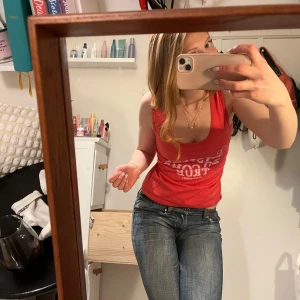 Röd linne med tryck - Säljer ett rosa linne med vitt tryck framtill. Linnet har en enkel design med breda axelband och rund halsringning. Perfekt för en temafest eller liknanade.