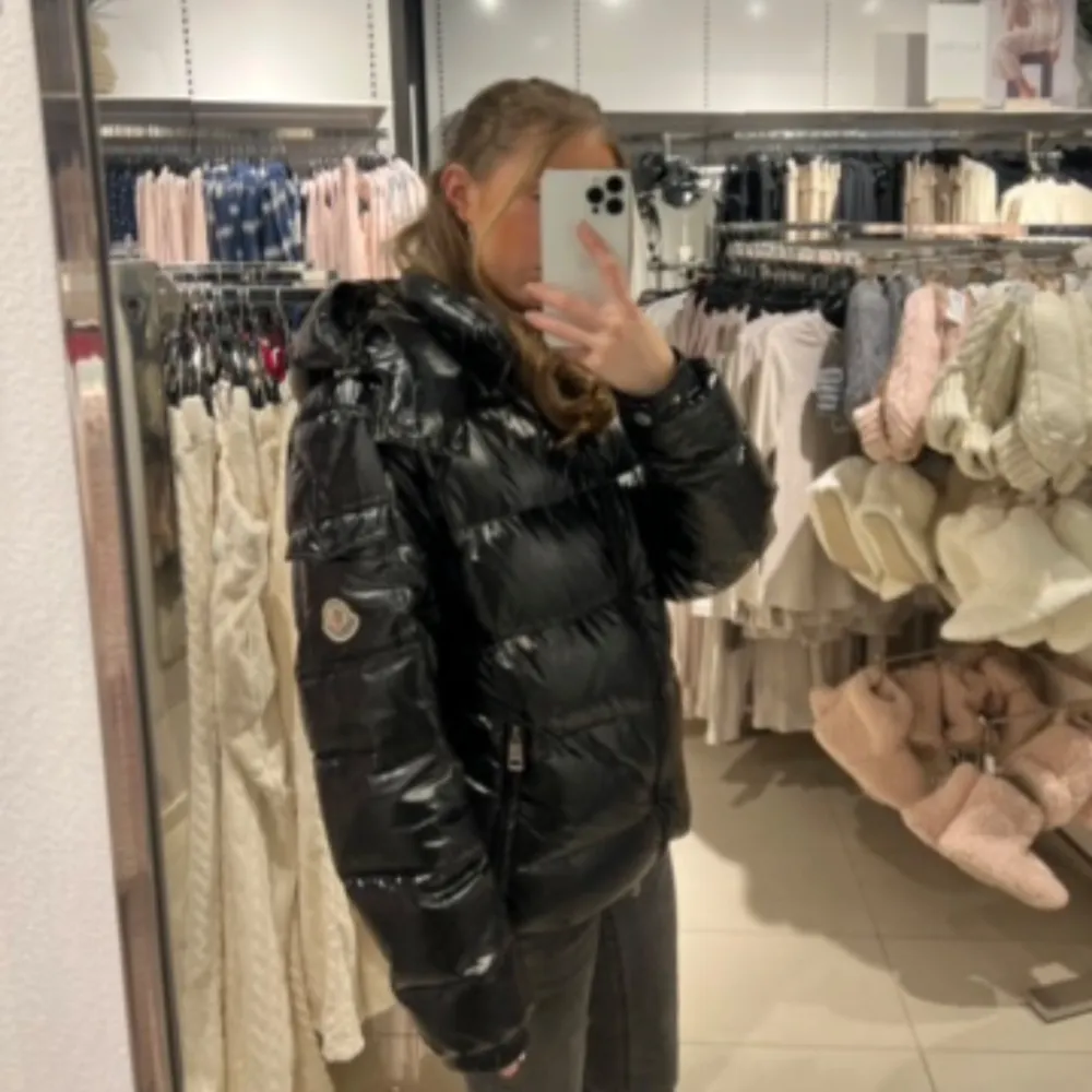Säljer en svart pufferjacka från Moncler med huva och dragkedja. Jackan har en glansig yta och är perfekt för kyligare väder. Den har långa ärmar och en normal passform. Perfekt för att hålla sig varm och stilren.. Takit.