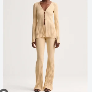 Avora set- slutsåld överallt 🫶🏼 - Snygg beige ribbad topp med lång ärm och v-ringning. Toppen har dekorativa knappar framtill och en stilren design som passar perfekt till både vardag och fest. Perfekt för höst och vår!