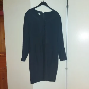 Svart klänning från Laura Ashley - Elegant svart klänning från Laura Ashley med långärmad design. Klänningen har en klassisk siluett och en dragkedja i ryggen för enkel påklädning. Perfekt för en stilren look.