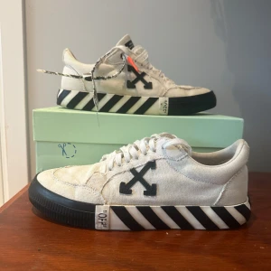 Vita sneakers med svarta detaljer från Off-White - Snygga vita sneakers från Off-White med svarta pilar på sidan och randig sula. Skorna har snörning och en unik design med en röd detalj på hälen. För överigt har skorna inte används så mycket men säljer dem till en billig peng då ny pris är på 2 800 kr. Och säljare dem nu för 1000 kr.  
