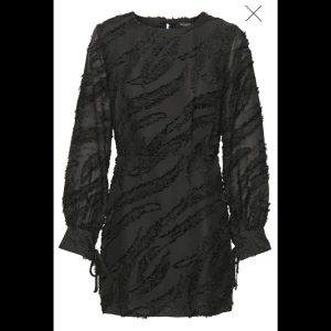 Svart klänning från SOAKED - Snygg svart klänning från SOAKED med ett unikt mönster och långa ärmar. Klänningen har en halvöppen rygg och en normal passform. Storlek XS