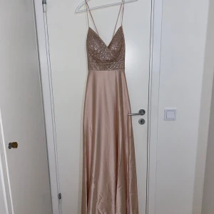 Champagnefärgad långklänning med paljetter - Hej tjejer, säljer denna snygga maxiklänning då jag bara har använt den en gång och använder inte den mer. Den passar utmärkt för dig som tar studenten och ska på bal eller kanske för ett bröllop. Den är i storlek 36. 
