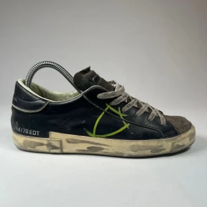 Svarta sneakers från Philippe Model - Snygga svarta sneakers från Philippe Model med grå snörning och en distinkt grön detalj på sidan. Skorna har en sliten look med en smutsig sula som ger dem en unik stil. Perfekta för en avslappnad och trendig look. 8/10 i skick bara lite smutsiga men såklart går de ju bort. Skorna e köpta för 3500 och säljer för 1500. Du får med en box men tyvärr ingen dust bag. Dm för köp!!