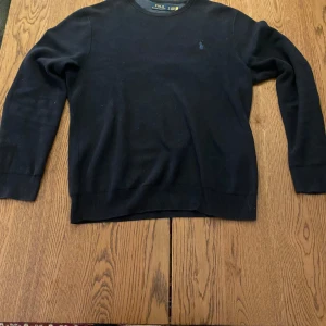 Ralph lauren stickad tröja - En tröja av god kvalitet och gott skick ifrån Polo Ralph Lauren. Tröjan är i en blå färg med en ljusare blå broderad logga. Den har krympt i tvätten och sitter nu mera som M/L men var tidigare en XL. 