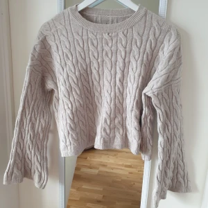 Ljusgrå kabelstickad tröja - Tröjan har en klassisk design med långa ärmar och rund halsringning. Perfekt för kyligare dagar och passar till många olika outfits.