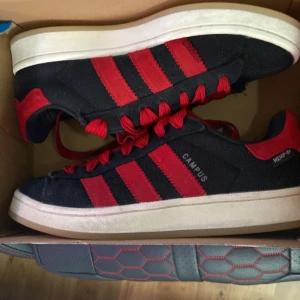 Svarta och röda Adidas Campus sneakers - Snygga Adidas Campus sneakers i svart med röda detaljer och snörning. Skorna har en klassisk design med tre röda ränder på sidan och en vit sula. Perfekta för en stilren look. Sulan är lite smutsig därför priset ny pris 1499 sek. Gamla snörerna är sönder. Namnet på skorna är TKO black power red