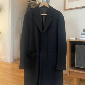 Svart rock från Acne Studios - Säljer en stilren svart rock från Acne Studios. Rocken har en klassisk design med långa ärmar och knappar framtill. Perfekt för en elegant look. Passar bra till både formella och avslappnade tillfällen.