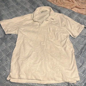 Vit t-shirt från A Day's March - Säljer en stilren vit frotté T-shirt  från A Day's March i storlek M. T-shirten har en klassisk krage och en bröstficka. Perfekt för en avslappnad look under sommaren !