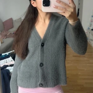 Grå kofta med knappar - Säljer en mysig grå kofta med knappar framtill. Koftan har en mjuk och fluffig textur, använt en gång!