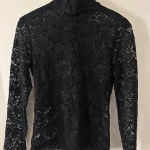 Svart spets polotröja från Whyred - Säljer en elegant svart spets polotröja från Whyred. Tröjan har långa ärmar och en vacker spetsdesign som ger en stilren look. Perfekt för att lägga till en touch av elegans till din garderob.