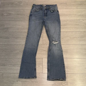 Blå jeans med bootcut - Snygga blå jeans med bootcut och en sliten detalj på ena benet. De har en klassisk femficksdesign och en låg midja. Perfekta för en avslappnad stil.läpp glans på fickor som går bort med tvål o vatten(priset går o diskutera 