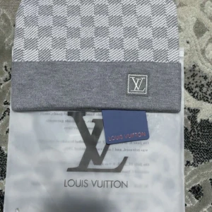 Grå rutig mössa  - Snygg grå mössa med ett klassiskt rutigt mönster. Mössan har en broderad logga framtill och är perfekt för att hålla dig varm med stil.