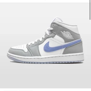 Nike Jordan 1 'Wolf Grey' Mid - Snygga Nike Jordan 1 'Wolf Grey' Mid i en stilren kombination av grått, vitt och ljusblått. Skorna har en klassisk design med snörning och den ikoniska Nike-loggan på sidan. Perfekta för dig som vill ha en stilren och sportig look.