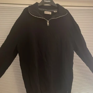 Svart tröja med dragkedja från Jack & Jones - Säljer en stilren svart tröja från Jack & Jones med halv dragkedja. Perfekt för en avslappnad look. Tröjan har långa ärmar och är tillverkad i ett mjukt material.