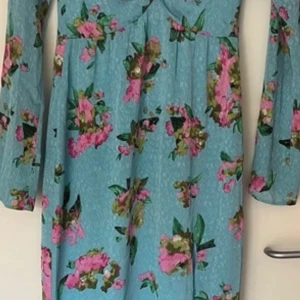 Blommig långärmad klänning - Säljer en superfin blommig klänning från Adoore  med lappari ljusblått med rosa och gröna blommor. Klänningen har långa ärmar och en bekväm passform, perfekt för vår och sommar. Den är gjord i ett mjukt och skönt material som känns härligt mot huden.