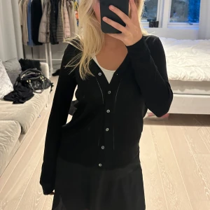 Svart kofta med knappar - Säljer en snygg svart kofta med knappar framtill. Den har en klassisk design med långa ärmar och en v-ringad hals. Perfekt för både vardag och festliga tillfällen. Märket är Zara och storlek S, den är i jättebra skick! 