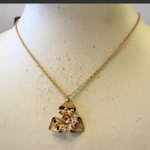 Guldhalsband med unikt hänge - Säljer ett elegant guldhalsband med ett unikt hänge. Hänget har en cool geometrisk design med tre triangulära former som möts i mitten, dekorerade med små guldkulor. Perfekt för att ge en touch av glamour till vilken outfit som helst!