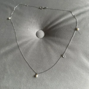 Silverhalsband med pärlor - Säljer ett elegant silverhalsband med små vita pärlor. Halsbandet har en tunn kedja och fyra jämnt fördelade pärlor som ger en stilren look. Sterlingsilver 925.